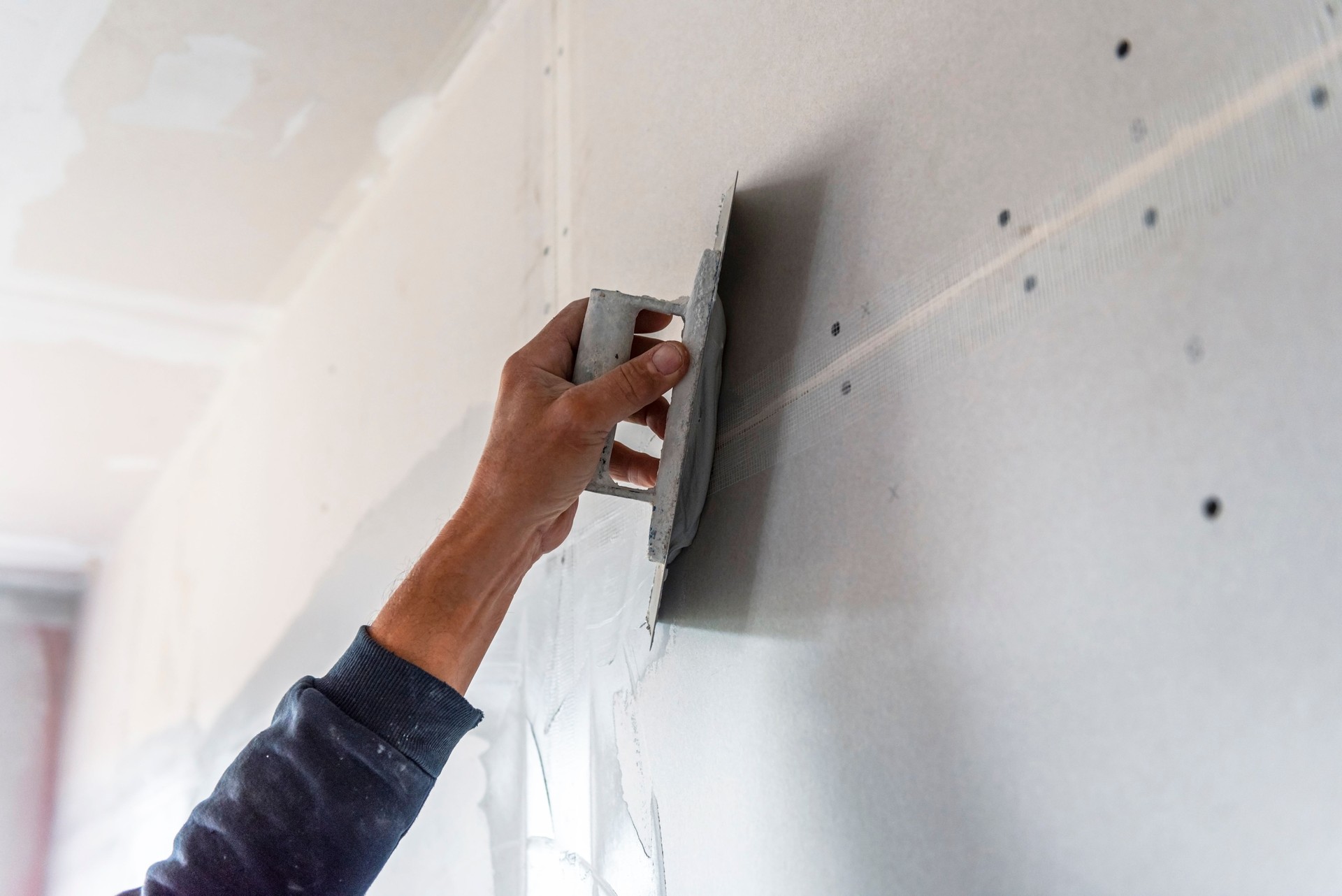 Old manual worker with wall plastering tools renovating house.